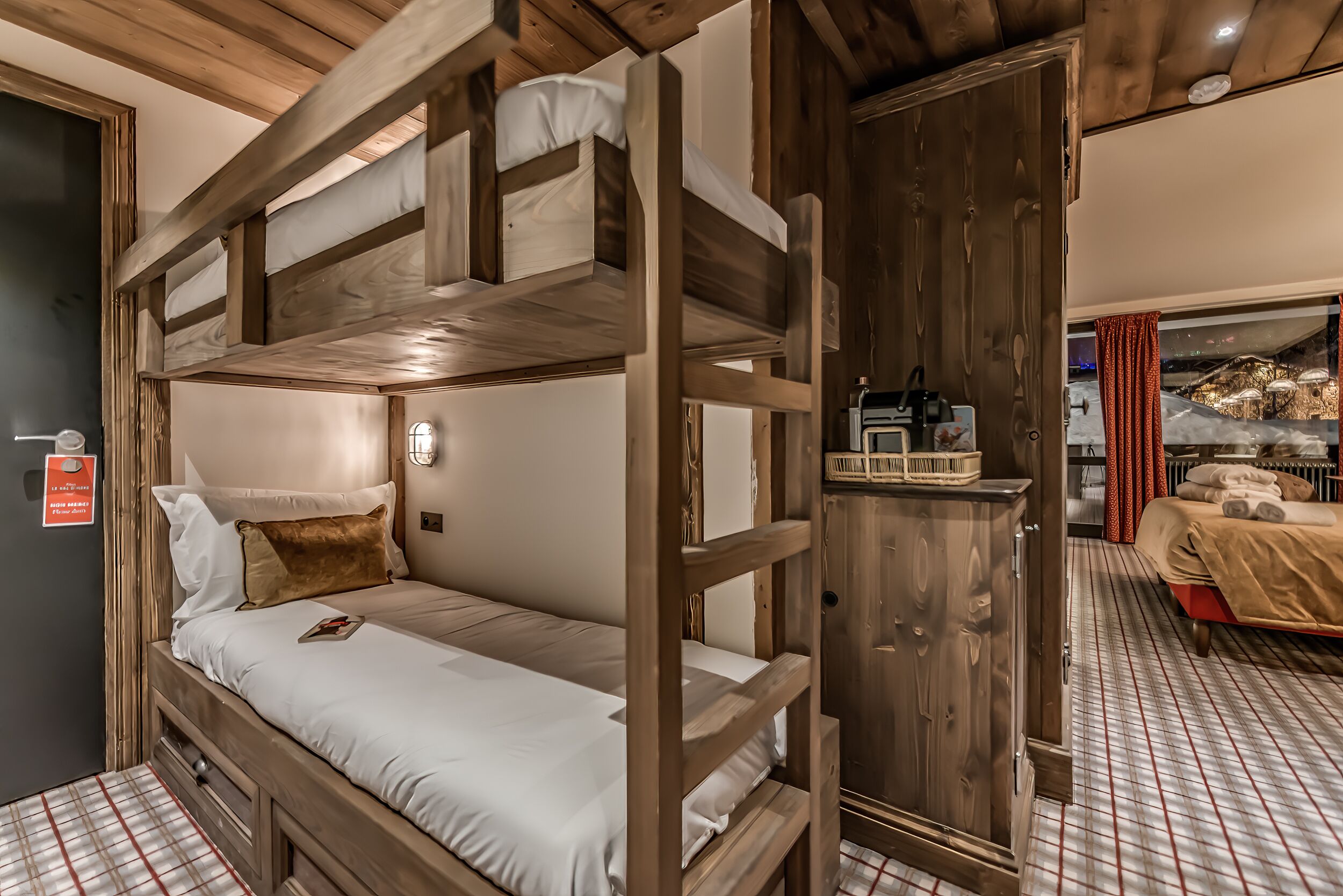 A bunk bed room with a wooden wardrobe and a small table with a basket.