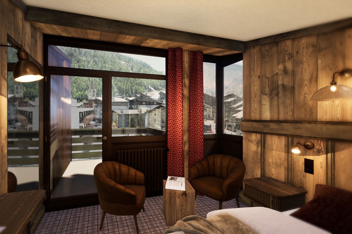 Una habitación acogedora con paredes de madera, un ventanal grande, dos sillones, una cama y una mesita.