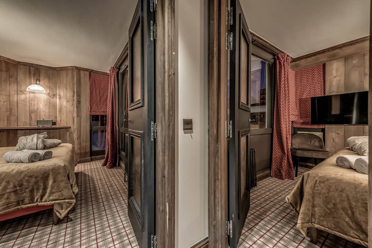 A hotel room with two beds, a TV, and a wooden wall.