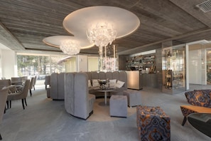 A modern lounge area with a sectional sofa, ottomans, and a bar area with shelves of bottles. - Hotel Rosengarten (Pinzolo)