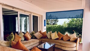 A modern living room with a curved sofa set, a glass coffee table, and a view of greenery outside. - Villa Dar Jbila (Tangier)