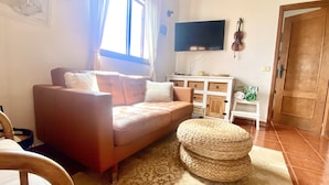 Una sala de estar con sofá, reposapiés y un televisor de pantalla plana montado en la pared.