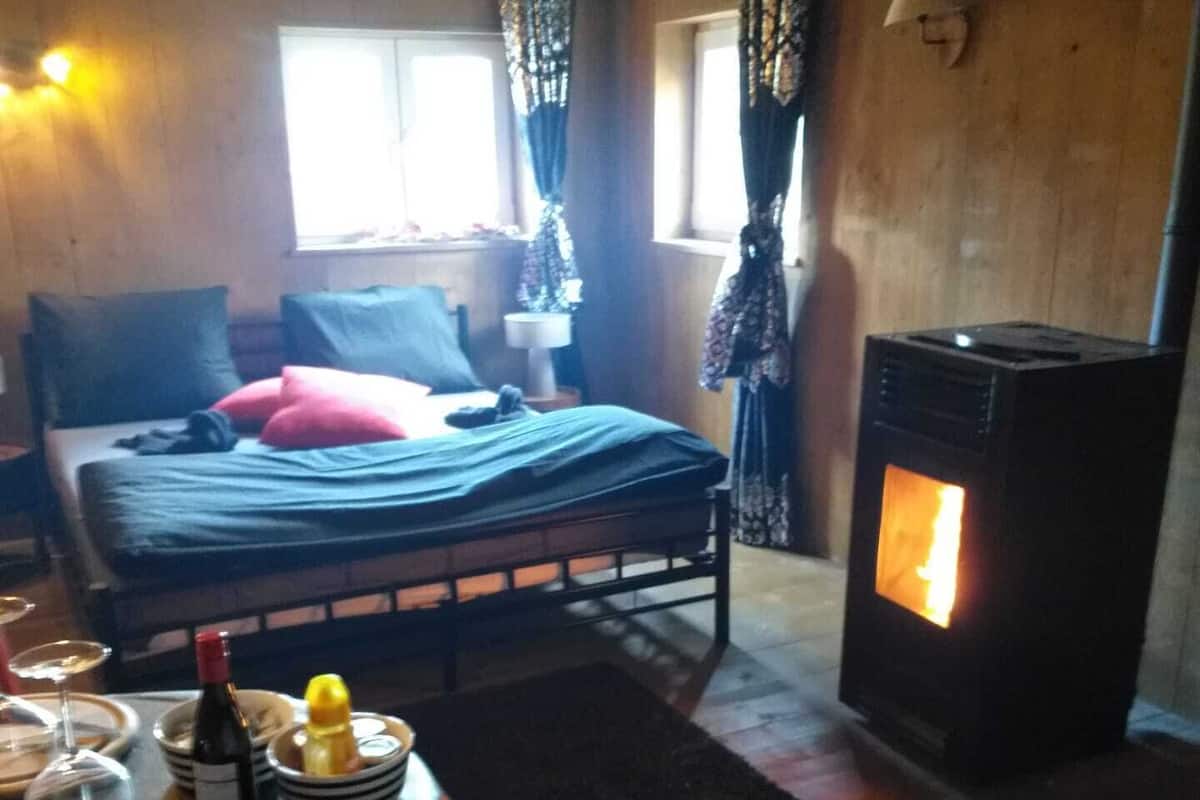 Une pièce chaleureuse avec un lit, une table dressée pour le repas et un poêle à bois.