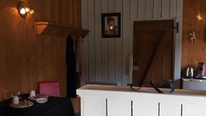A wooden interior with a dining table set for two, a red chair, and a white counter with a sink. - B&B La Petite Suisse (Malmedy)