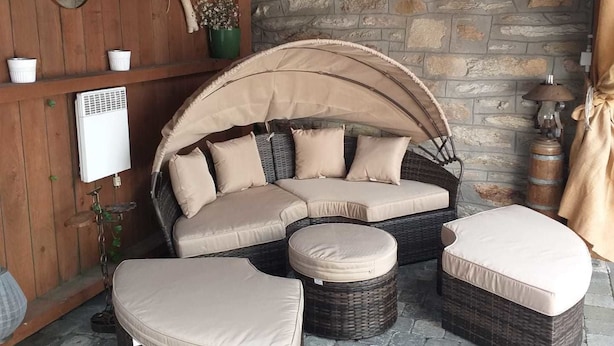 A cozy outdoor seating area with a curved sofa and ottomans, a stone wall, and a wooden ceiling. - B&B La Petite Suisse (Malmedy)