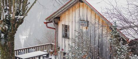 Ein rustikales Holzhaus mit einem Schild, auf dem 'LOVE NEST' steht, und einer mit Schnee bedeckten Deck mit Bänken.