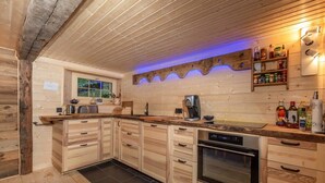 A kitchen with wooden cabinets, a built-in oven, a coffee maker, and a shelf with bottles. - Heidi Chalet Alps - Unique Experience - Authentic Part (Rossinière)