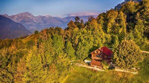 Eine Holzhütte in einer bewaldeten Bergregion mit freiem Blick auf ferne Berge.