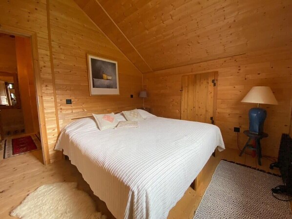 Ein Schlafzimmer einer Holzhütte mit Bett, Nachttisch, Lampe und einem Bild an der Wand.