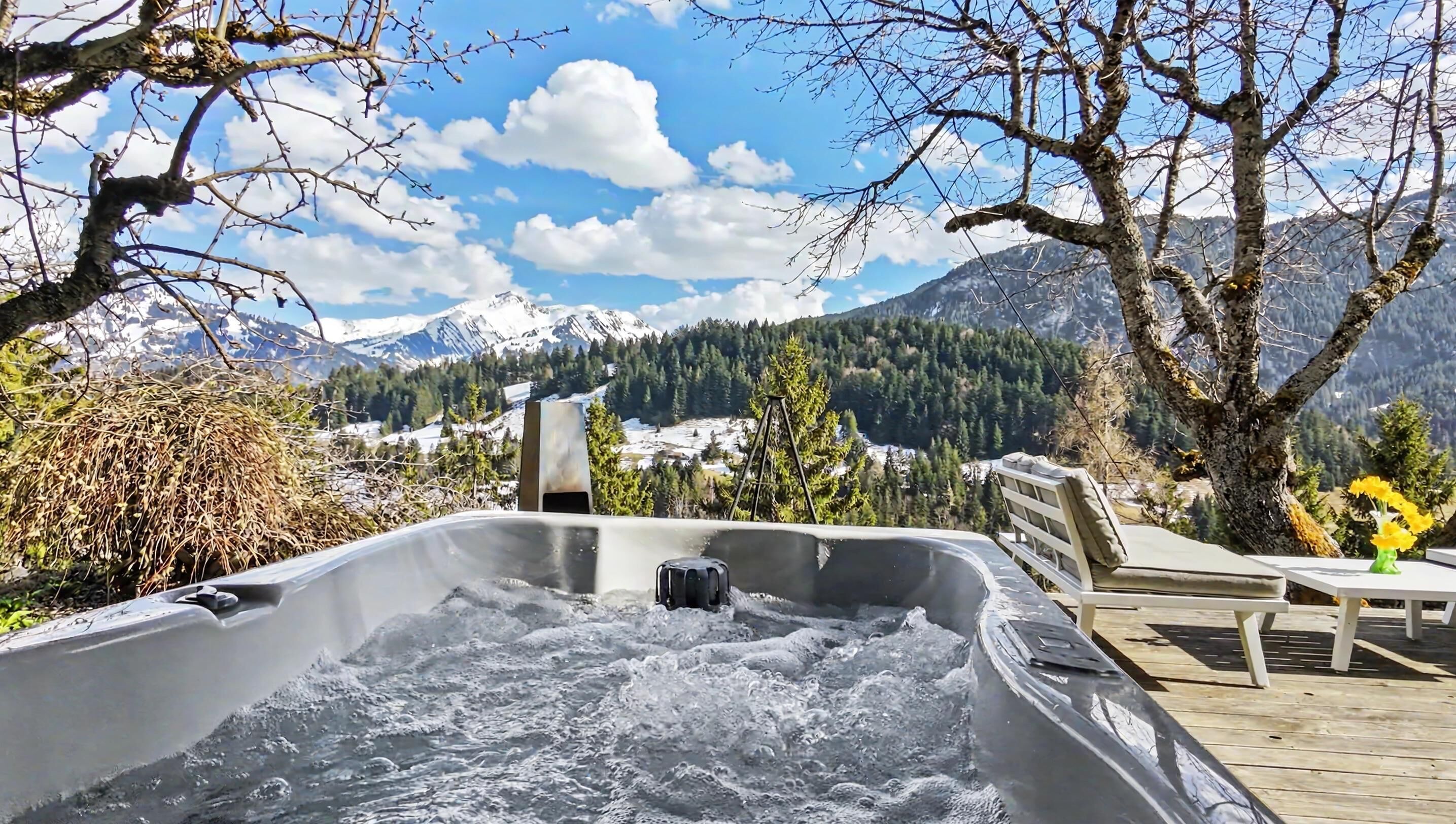 A hot tub with a mountain view, a wooden deck, and a chair.