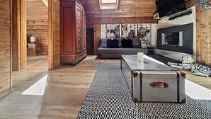 A cabin interior with wooden walls, a sofa, a TV, and a suitcase. - Paradise View - 5 BR Gstaad Paradise View Chalet with Outdoor Jacuzzi (Rougemont)