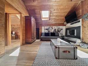 A cabin interior with wooden walls, a sofa, a TV, and a suitcase.