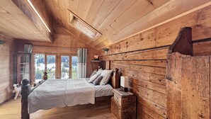 A wooden cabin bedroom with a bed, bedside table, and a view of the outdoors. - Paradise View - 5 BR Gstaad Paradise View Chalet with Outdoor Jacuzzi (Rougemont)