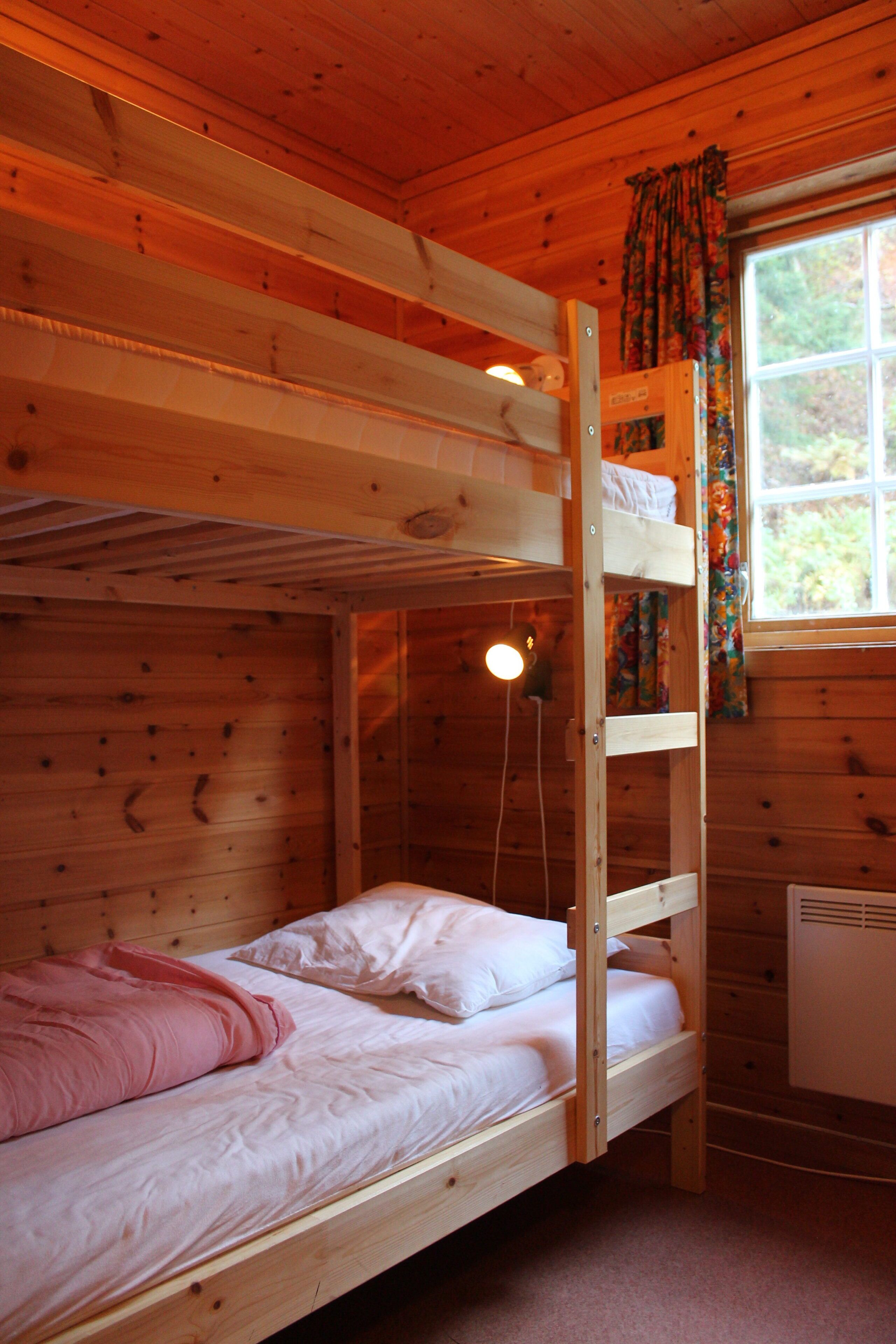 A bunk bed room with a window, wooden walls, and a heater.