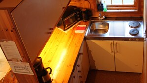 A compact kitchen with wooden cabinets, a sink, a stove, and a window with a checkered valance. - Hjelledalen Hyttesenter (Stryn)
