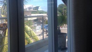 A view from a window with a metal railing, overlooking a street with parked cars and a building with a white roof. - Lili House (San Andrés)