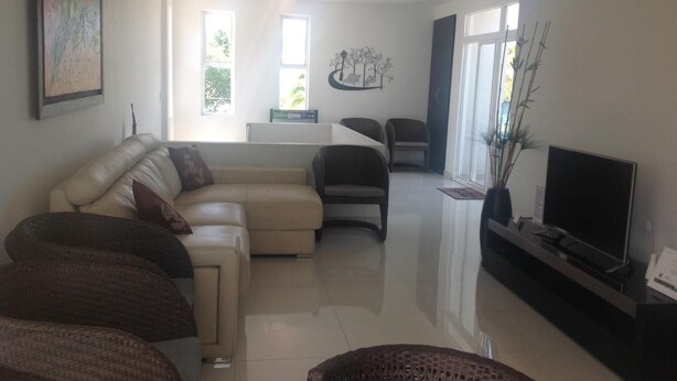 A modern living room with a sectional sofa, a flat-screen TV, and a dining area with chairs. - Lili House (San Andrés)