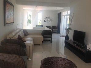 A modern living room with a sectional sofa, a flat-screen TV, and a dining area with chairs. - Lili House (San Andrés)
