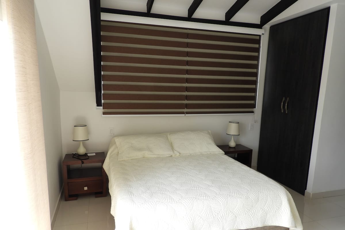 Ein Schlafzimmer mit einem Bett, zwei Nachttischen mit Lampen, einem Fenster mit Jalousien und einem Kleiderschrank.