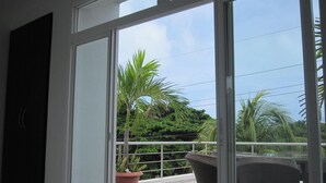 A balcony with a glass door, a potted plant, and a wicker chair. - Lili House (San Andrés)