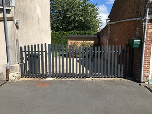 Une entrée fermée par un portail et protégée par une clôture en métal, un mur de briques et une boîte aux lettres verte.