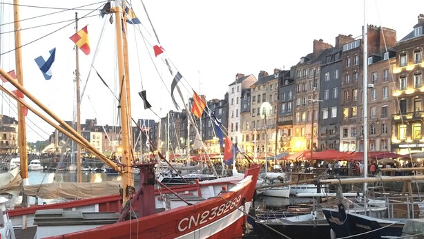 Ein Hafen mit mehreren vertäuten Booten, darunter ein rotes Boot mit der deutlich sichtbaren Nummer CN2-5899, und mehrstöckige Gebäude im Hintergrund.