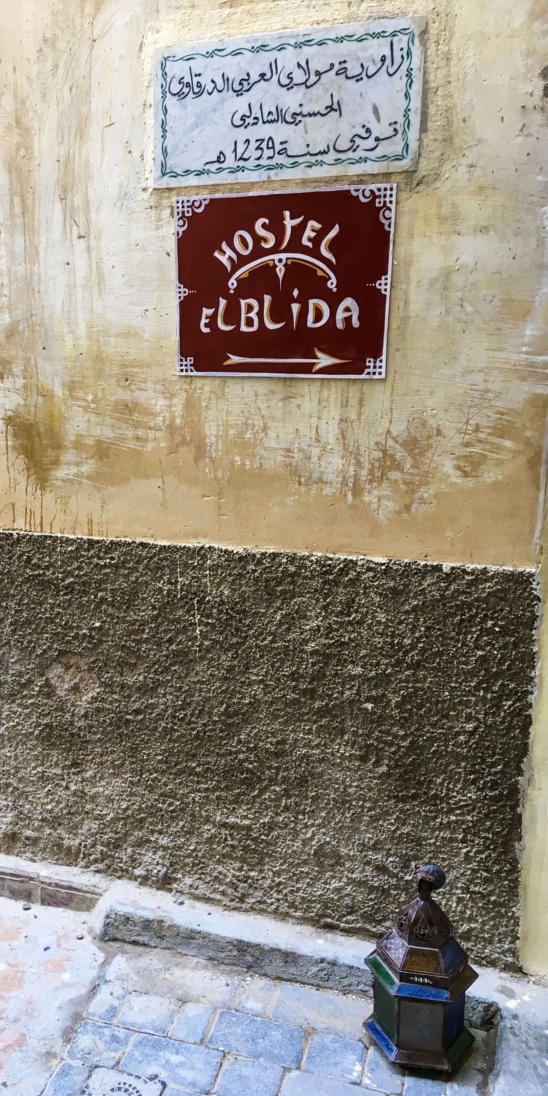 Una pared con un letrero que indica un hostal llamado "Elbida" y otro letrero con texto en árabe.