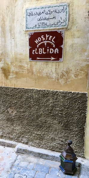 A wall with a sign indicating a hostel named "Elbida" and another sign with Arabic text.