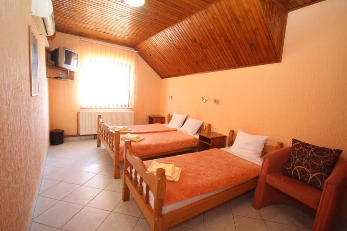 Una habitación con dos camas de madera, un sofá rojo, un televisor sobre una estantería y una ventana con cortinas.