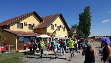 Un grupo de personas reunidas frente a un edificio amarillo con techo rojo, posiblemente en un evento o reunión comunitaria.