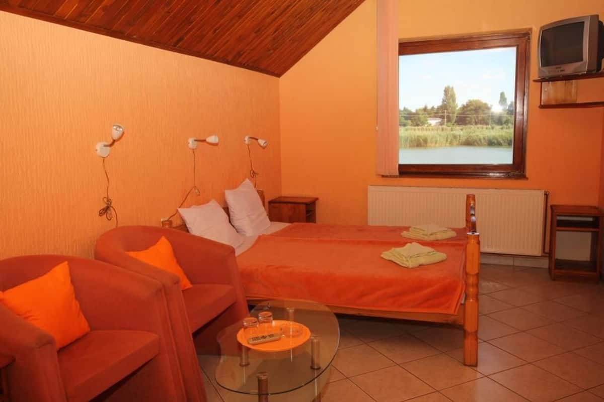 Un dormitorio con cama, sofá, una mesita de vidrio y ventana con vista a zonas verdes.