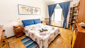 A bedroom with a bed, a nightstand, a wooden dresser, a bookshelf, and a window with curtains. - Lovely apartment for 6 guests with WIFI, TV and balcony (Lucca)