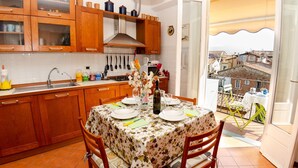 A kitchen with wooden cabinets, a dining table set for two, and a view of the city through an open door. - Lovely apartment for 6 guests with WIFI, TV and balcony (Lucca)