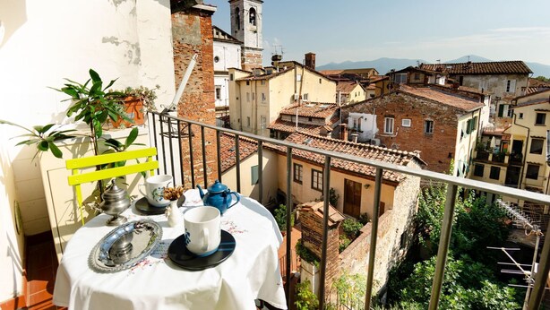 A balcony with a table set for two, overlooking a historic town with terracotta roofs and a church tower. - Lovely apartment for 6 guests with WIFI, TV and balcony (Lucca)
