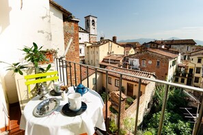 Ein Balkon mit Tisch für zwei Personen, mit Blick auf eine historische Stadt mit Terrakotta-Dächern und einem Kirchturm.
