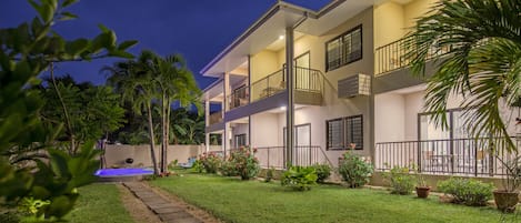 A two-story residential building with a well-maintained lawn, potted plants, and a visible swimming pool.