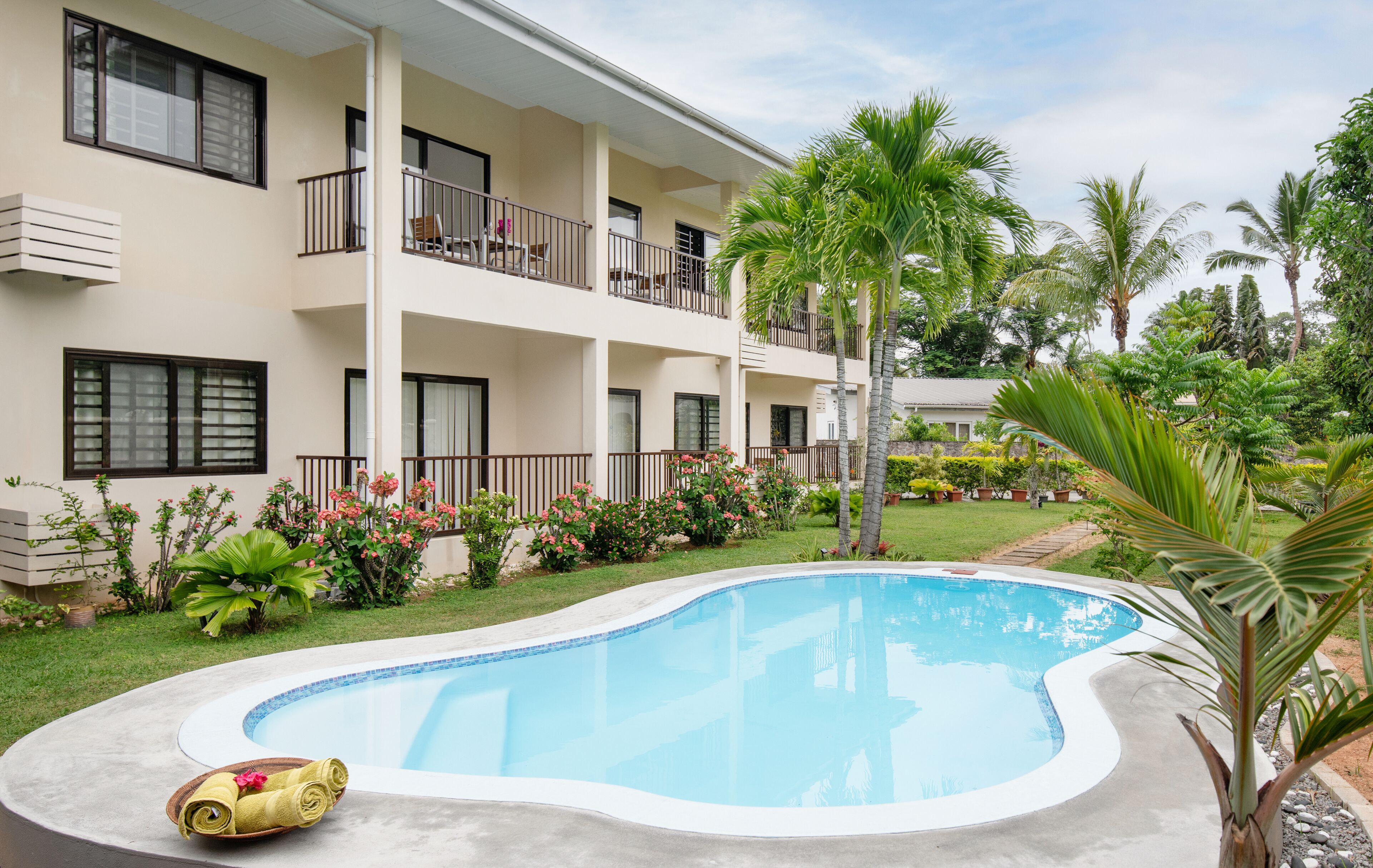 A hotel with a swimming pool, balconies, and tropical landscaping.