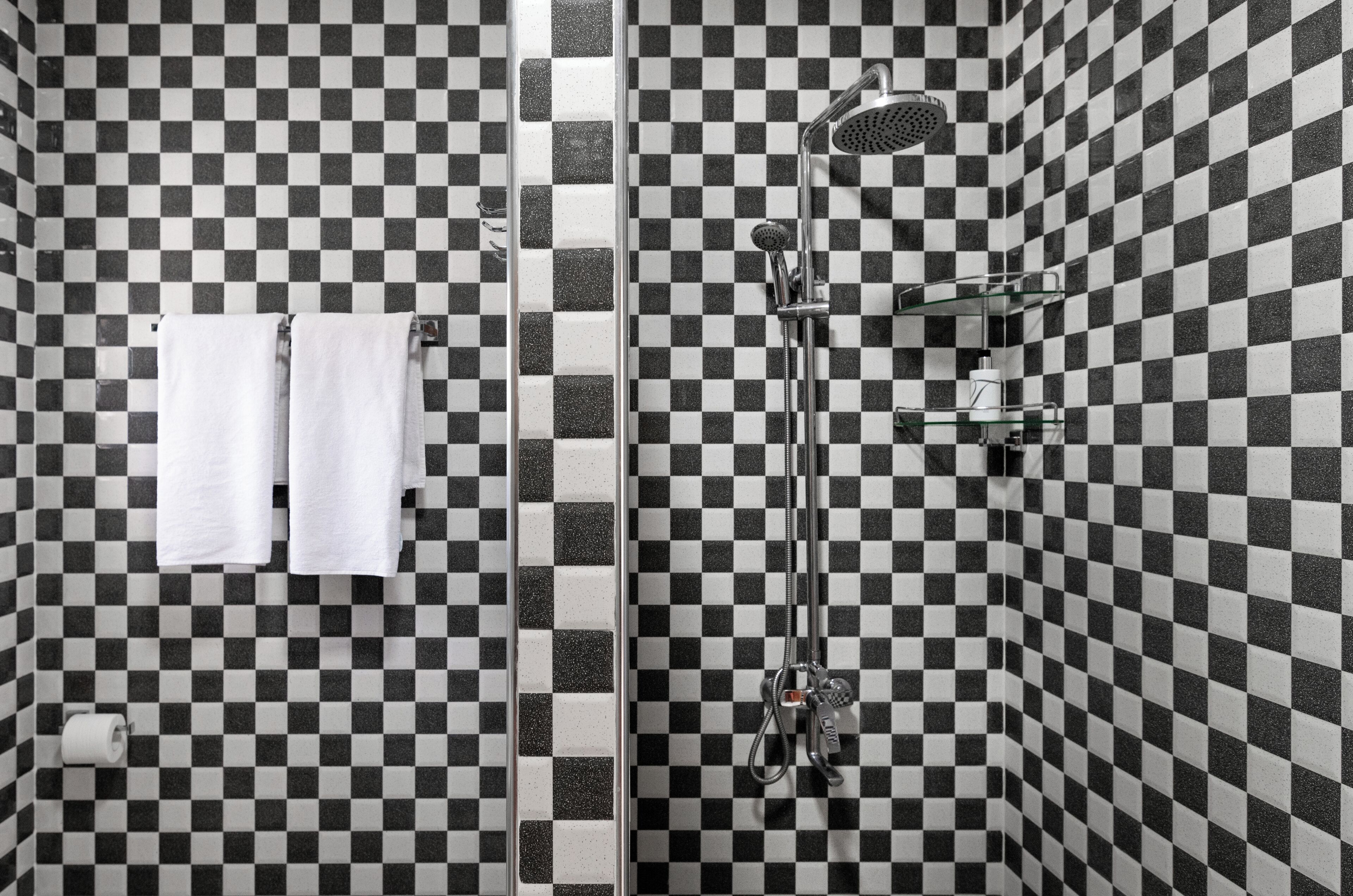 A bathroom with a checkered tile pattern, a shower with a handheld showerhead, and two white towels hanging on a rack.