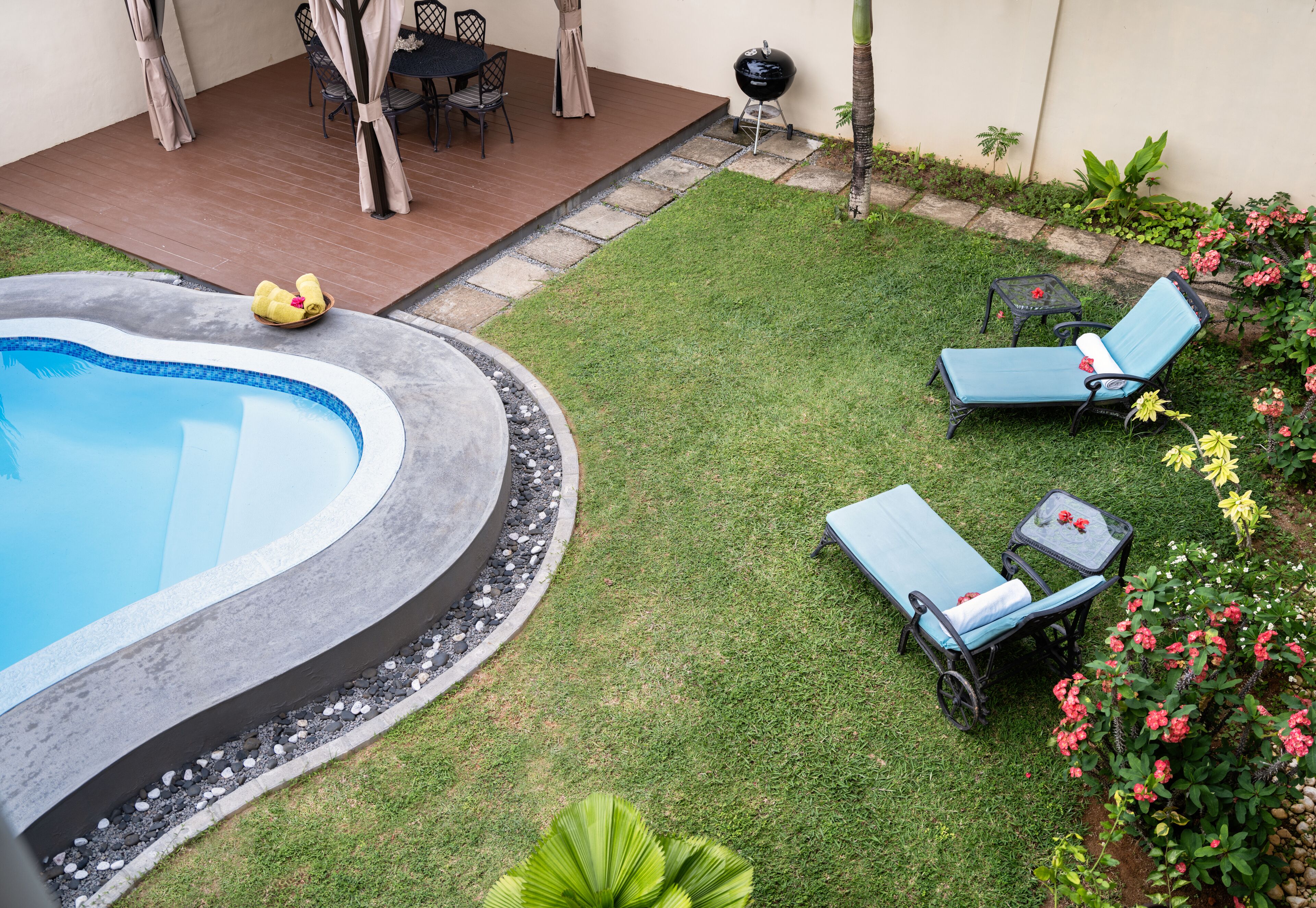 A backyard with a swimming pool, two lounge chairs, a barbecue grill, and a dining area with chairs and a table.