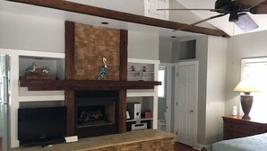 Una sala de estar con chimenea de piedra, vigas de madera, ventilador de techo y televisor.