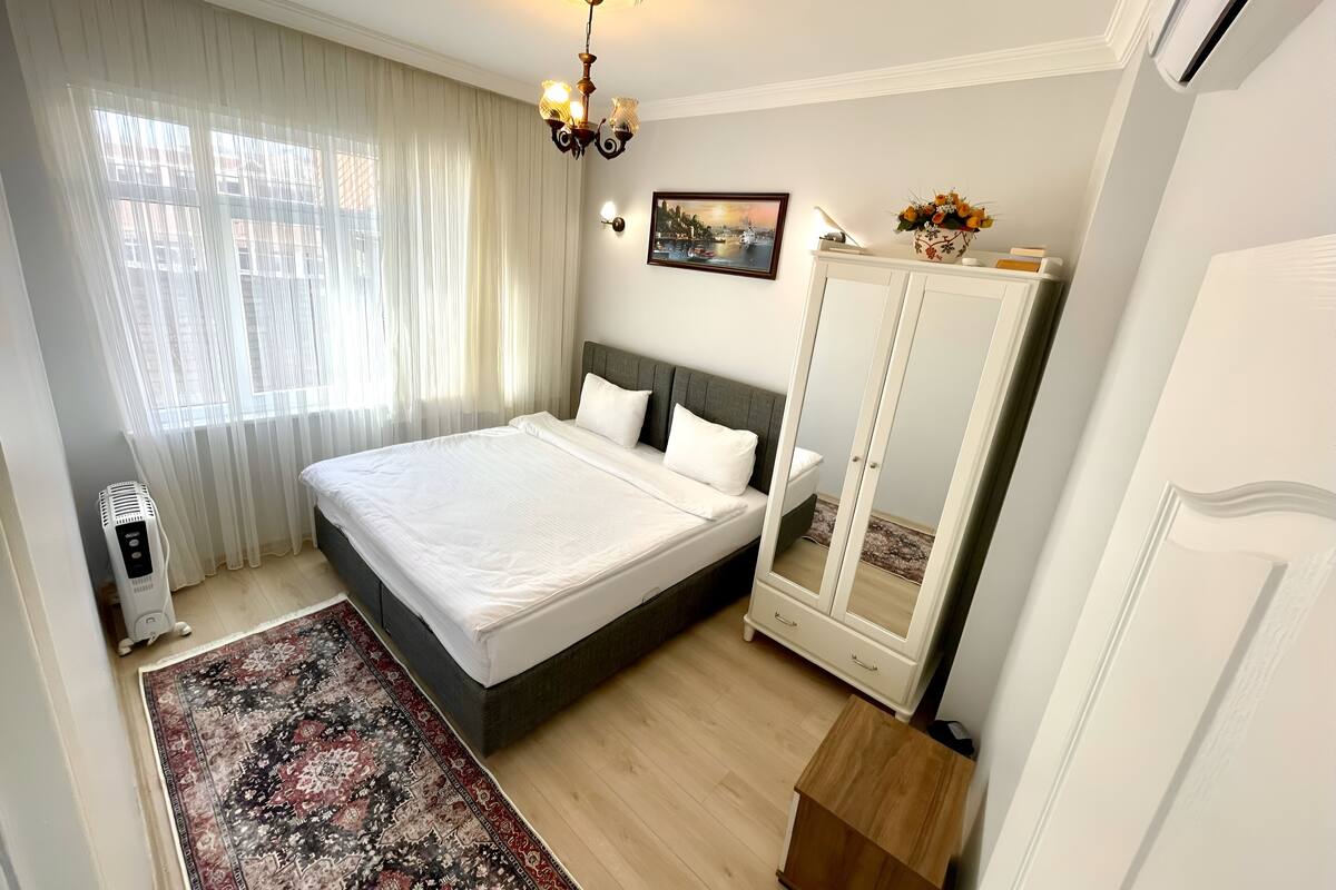 Quarto com cama, guarda-roupa, radiador, tapete e lustre.