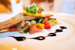 A close-up of a dish with grilled fish, vegetables, and a garnish on a white plate. - Hotel Krimmlerfälle (Krimml)