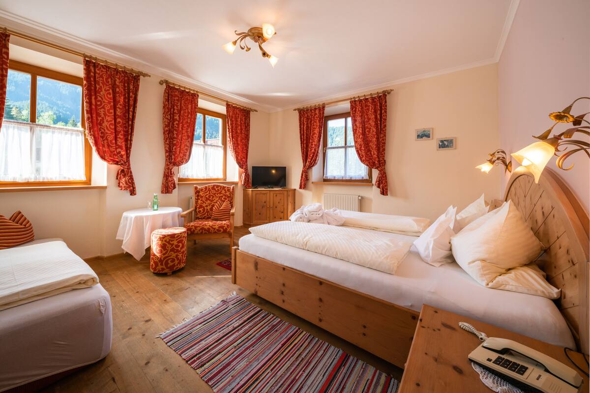 A bedroom with two beds, a television, a wooden cabinet, and a small table with a lamp.
