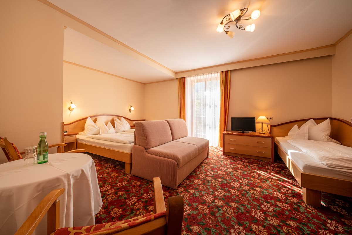 A hotel room with two beds, a sofa, a small table with a bottle, and a TV.