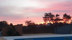 Een zwembad met een houten terras, omringd door een lage muur en bomen, onder een zonsondergang.