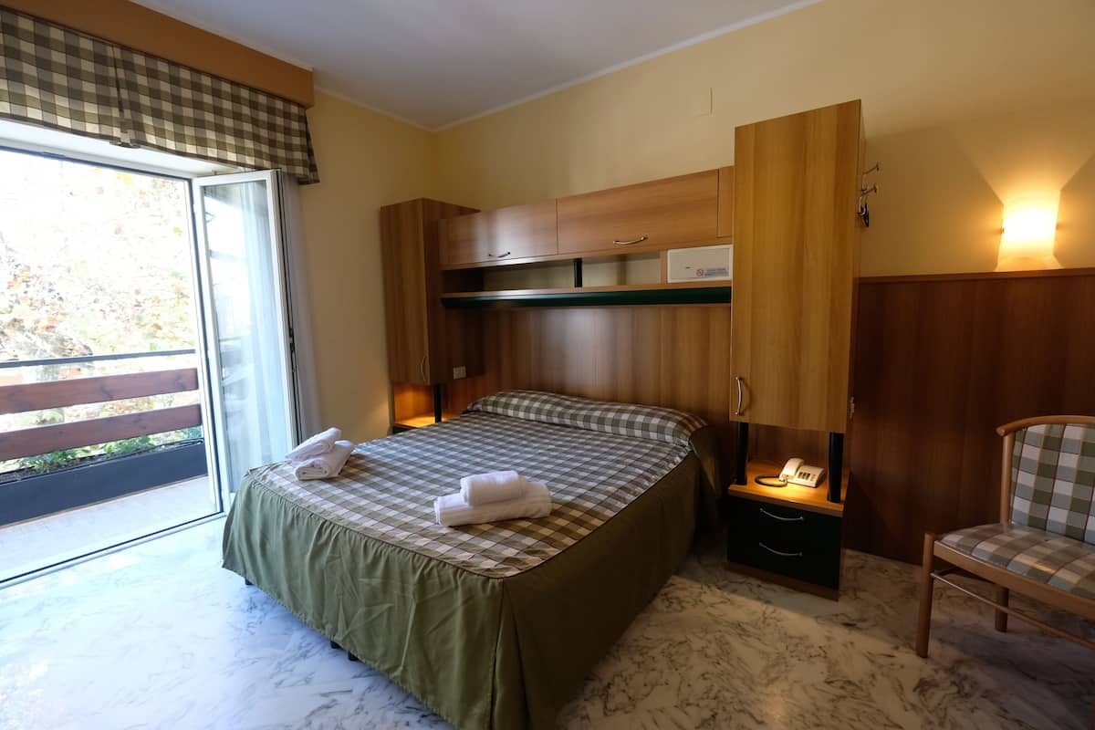 A bedroom with a bed, a nightstand, a chair, a wardrobe, and a window with a view.