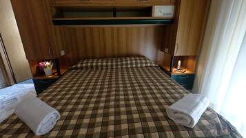 A hotel room with a checkered bedspread, two bedside tables, a nightstand, a small cabinet, and a window with curtains.