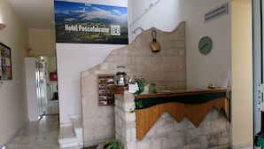 A reception desk with a stone wall, a kettle, a clock, and a poster of a mountain landscape. - Hotel Pescofalcone (Caramanico Terme)
