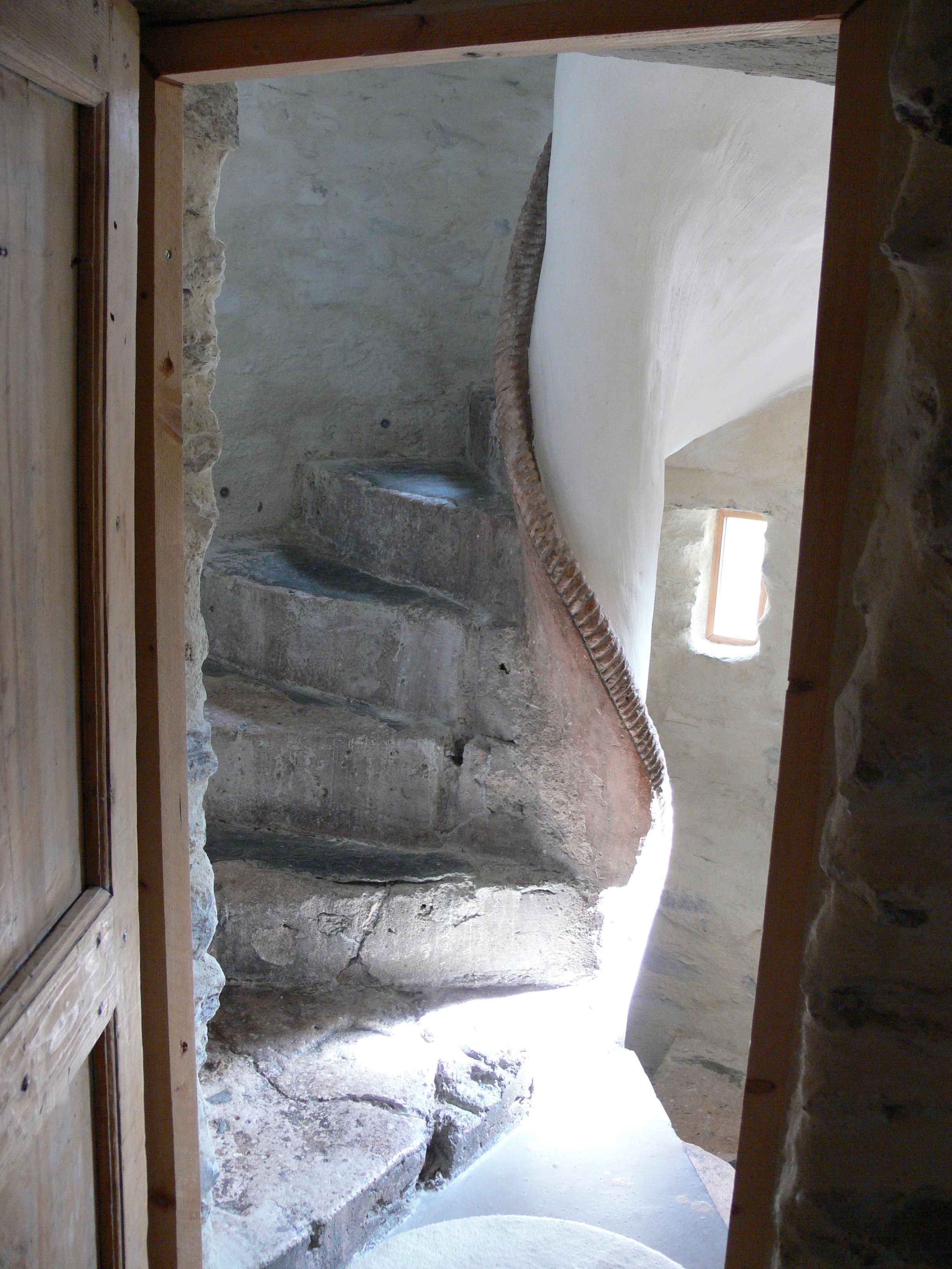 Una escalera de piedra que conduce a un piso superior, con un marco de puerta de madera a la izquierda y una ventana a la derecha.