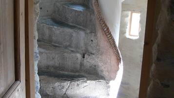Una escalera de piedra que conduce a un piso superior, con un marco de puerta de madera a la izquierda y una ventana a la derecha.